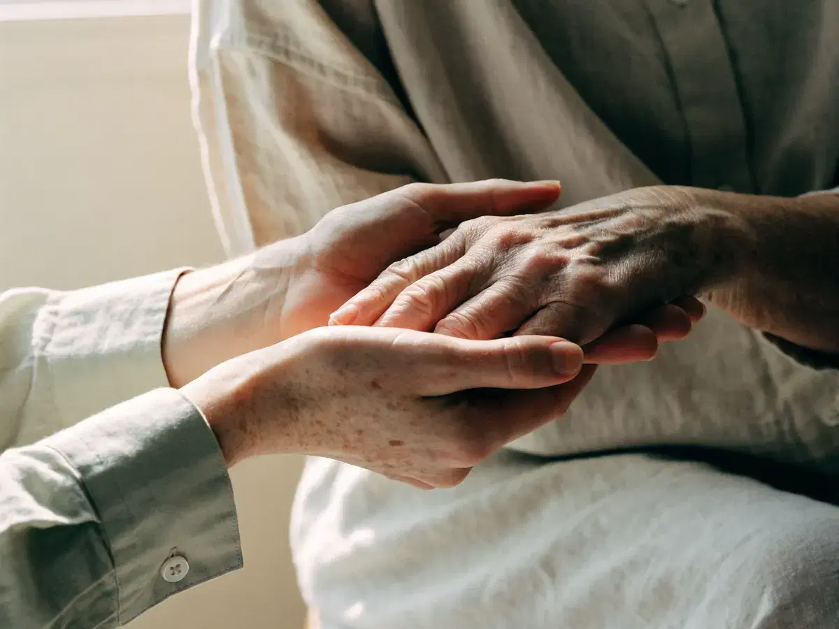 A practitioner holding an older patient's hand during care